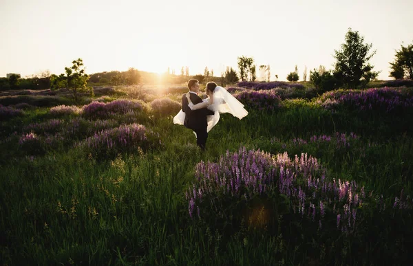 Nygifta Står Mitt Ett Blommande Fält Vid Solnedgången Brudgummen Håller — Stockfoto
