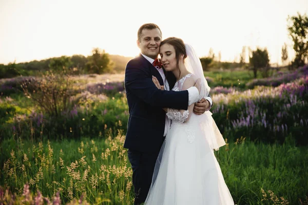 Bride and groom hugging at sunset.Happy bride and groom smiling.Happy bride and groom after the wedding ceremony.Wedding day.Beautiful young couple in a field with flowers,wedding day in the lives of young people