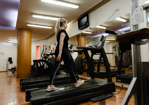 young girl in a sports uniform runs on a treadmill in the gym,one girl in an empty gym,girl losing weight in the gym