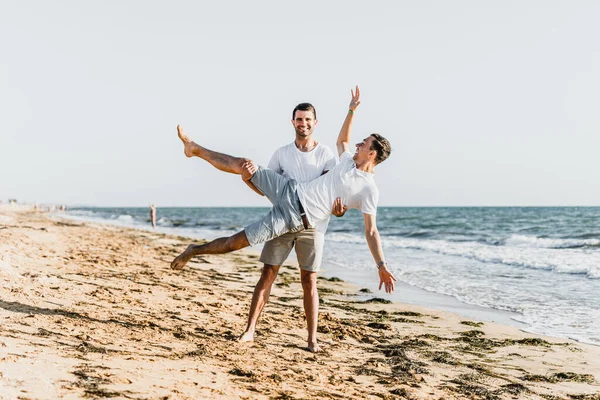 best friends cuddling on the beach,vacation with a friend at sea,fooling around with a friend,friend holds friend in his arms,walk along the beach,two nice guys,nice and lovely guys