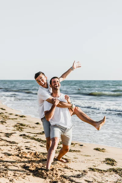 best friends cuddling on the beach,vacation with a friend at sea,fooling around with a friend,friend holds friend in his arms,walk along the beach,two nice guys,nice and lovely guys