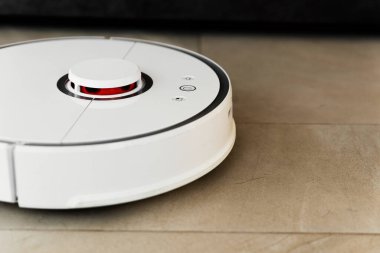 Temizlik sırasında robot elektrikli süpürge, beyaz robot elektrik süpürgesi döküntüleri temizliyor, elektrikli süpürge ile ev temizliği, elektrikli süpürge, elektrikli robot temizleme teknolojisi.