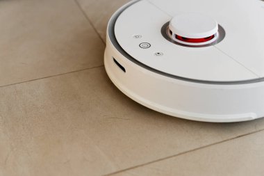 Temizlik sırasında robot elektrikli süpürge, beyaz robot elektrik süpürgesi döküntüleri temizliyor, elektrikli süpürge ile ev temizliği, elektrikli süpürge, elektrikli robot temizleme teknolojisi.