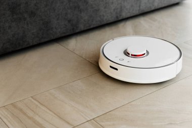 Temizlik sırasında robot elektrikli süpürge, beyaz robot elektrik süpürgesi döküntüleri temizliyor, elektrikli süpürge ile ev temizliği, elektrikli süpürge, elektrikli robot temizleme teknolojisi.