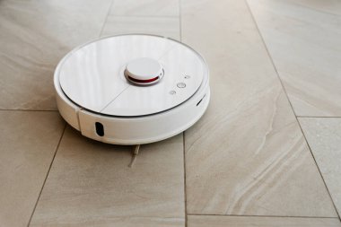 Temizlik sırasında robot elektrikli süpürge, beyaz robot elektrik süpürgesi döküntüleri temizliyor, elektrikli süpürge ile ev temizliği, elektrikli süpürge, elektrikli robot temizleme teknolojisi.