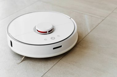 Temizlik sırasında robot elektrikli süpürge, beyaz robot elektrik süpürgesi döküntüleri temizliyor, elektrikli süpürge ile ev temizliği, elektrikli süpürge, elektrikli robot temizleme teknolojisi.