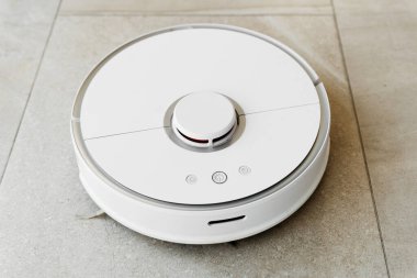 Temizlik sırasında robot elektrikli süpürge, beyaz robot elektrik süpürgesi döküntüleri temizliyor, elektrikli süpürge ile ev temizliği, elektrikli süpürge, elektrikli robot temizleme teknolojisi.
