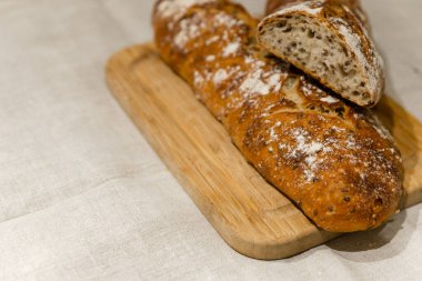 Çarşafların üzerinde taze ekmek, kesme tahtasının üzerinde ekmek, masada pişmiş ekmek, keten arka planda dilimlenmiş ekmek.