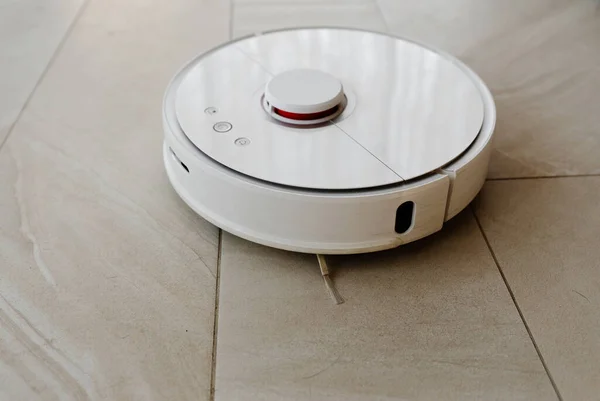 Robot vacuum cleaner during cleaning,white robot vacuum cleaner cleans the floor from debris,home cleaning with an electric vacuum cleaner,vacuum cleaner electric robot cleaning technology