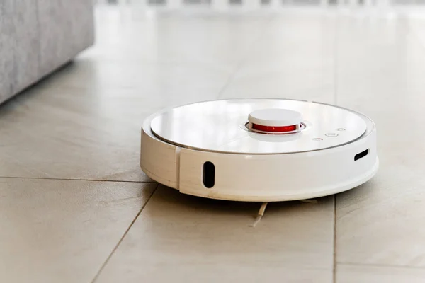 Robot vacuum cleaner during cleaning,white robot vacuum cleaner cleans the floor from debris,home cleaning with an electric vacuum cleaner,vacuum cleaner electric robot cleaning technology