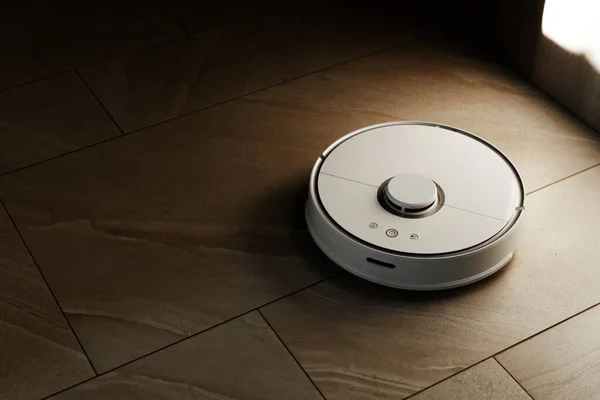 Robot vacuum cleaner during cleaning,white robot vacuum cleaner cleans the floor from debris,home cleaning with an electric vacuum cleaner,vacuum cleaner electric robot cleaning technology