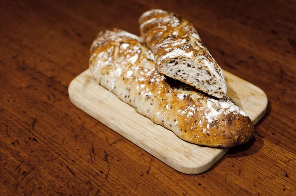 home baked fresh bread lying on a wooden table,two breads lie on a cutting board,branded home-baked bread,baguette with seeds,bran loaf