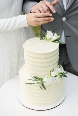 Beyaz ranzalı düğün pastası bir masanın üzerinde duruyor, gelin bir düğün pastası kesiyor, çiçekçilerle süslenmiş düğün pastası, düğün gününün sonunda bir düğün pastası kesiliyor, dışarıda pasta var.