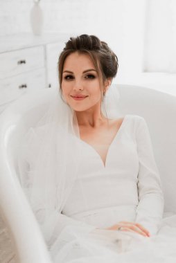 Genç gelin banyoda yatıyor, düğün günü gelini, gelinlikli güzel kız beyaz bir banyoda yatıyor, gelin portresi, düğün fotoğrafı çekimi, gelinlik, gelin elleriyle yüzüne dokunuyor.