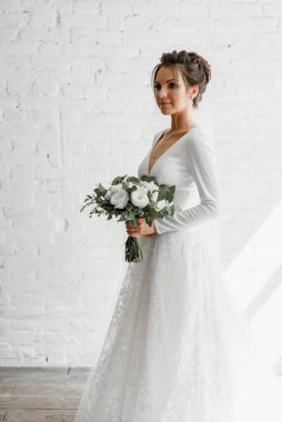 Gelin beyaz bir buket ile beyaz bir stüdyo tuğla arka planda, gelinlik kataloğu, güzel gelin damat, gelin portresi, güzel bir gelinlik içinde yalnız gelin bekliyor.
