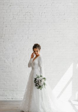 Gelin beyaz bir buket ile beyaz bir stüdyo tuğla arka planda, gelinlik kataloğu, güzel gelin damat, gelin portresi, güzel bir gelinlik içinde yalnız gelin bekliyor.