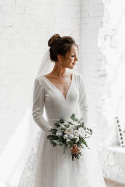 Gelin beyaz bir buket ile beyaz bir stüdyo tuğla arka planda, gelinlik kataloğu, güzel gelin damat, gelin portresi, güzel bir gelinlik içinde yalnız gelin bekliyor.