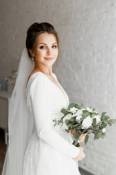 美丽的新娘 一束美丽的花朵迎面映衬着一堵白色的砖墙 漂亮新娘的华丽婚纱 时髦的婚纱 结婚花束 — 图库照片