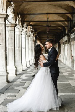 Düğün yürüyüşü sırasında mutlu gelin ve damat kucaklaşır. Hoş bir çiftin düğün günü. Yeni evlilerin güzel kıyafetleri.,