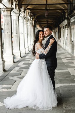 Düğün yürüyüşü sırasında mutlu gelin ve damat kucaklaşır. Hoş bir çiftin düğün günü. Yeni evlilerin güzel kıyafetleri.,