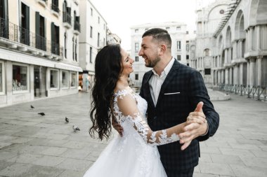 Gelin ve damat tarihi bir binanın arka planında, gelin ve damat eski Venedik şehrinin sokaklarında yürüyor, yeni evliler dans ediyor, Avrupa düğünü, karantina düğünü