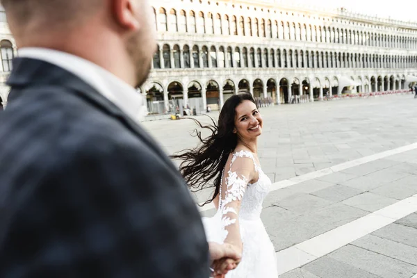 young and loving groom and bride hold hands and run down the street,newlyweds walk on the wedding day in the streets of Venice