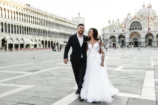 Düğün yürüyüşü sırasında mutlu gelin ve damat kucaklaşır. Hoş bir çiftin düğün günü. Yeni evlilerin güzel kıyafetleri.,