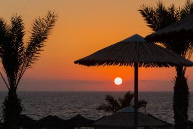Palmiye ağacı siluetleri ve plaj şemsiyesi ile Akdeniz günbatımı