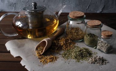 Ev yapımı eczacı. Doğal şifalı bitkiler. Cam kavanozlarda kurutulmuş otlar ve koyu ahşap yüzeyde çaydanlık. Çeşitli bitki çayları..