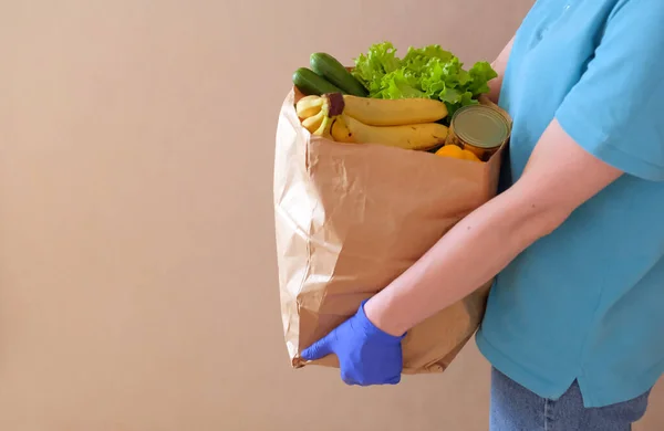 Volunteer in medical gloves delivers food in paper bag during virus outbreak, coronavirus pandemic.Side view.