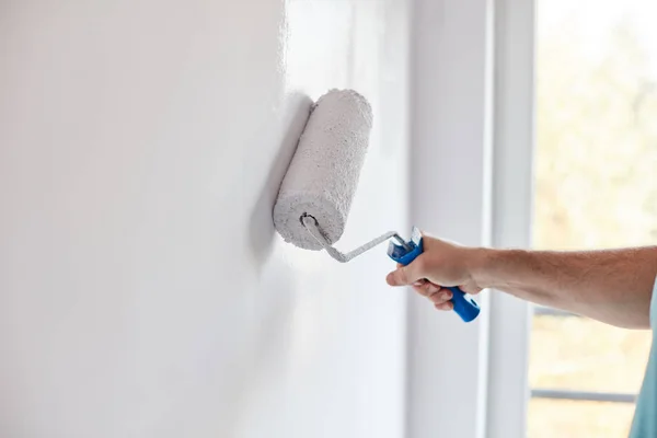 Male hand painting wall with paint roller. Painting apartment, r