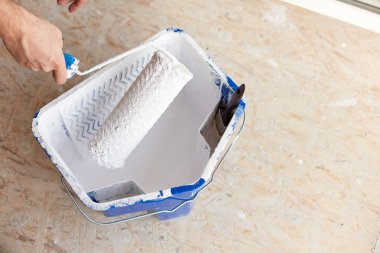 Beyaz boya fırça rulo tutan bir erkek el ile bir kova