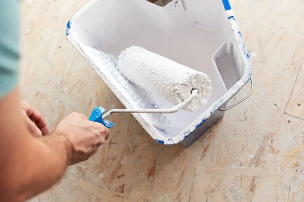 Egy vödör fehér festékkel egy férfi kezében egy ecset roller — Stock Fotó