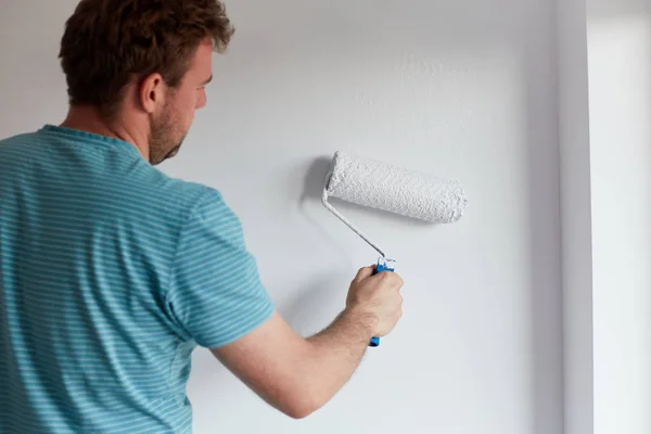 Jeune homme peignant un mur sur blanc dans une maison moderne — Photo