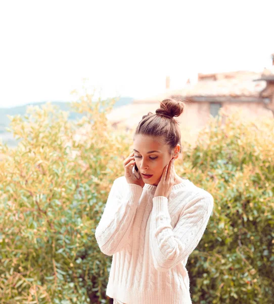 Πολύ όμορφη νεαρή γυναίκα στο λευκό πουλόβερ και εσώρουχα, μιλώντας στο τηλέφωνο, στέκεται στο μπαλκόνι. Τοσκάνη, Ιταλία. Μικρό βάθος πεδίου. — Φωτογραφία Αρχείου