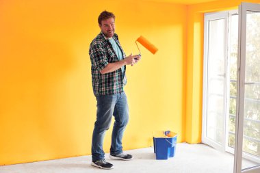 Genç bir adam modern bir evde ayçiçeği rengine duvar boyuyor.