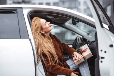Mutlu kızıl saçlı bir kız Noel hediyesinin tadını çıkarır. Ceketli güzel bir kadın yeni yıl hediyesiyle arabada oturuyor.