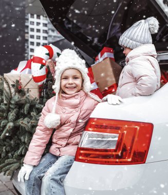Christmas, Xmas, child, happiness concept - cute happy girl in winter clothes sitting with gifts and fir tree after shopping and waiting her parents