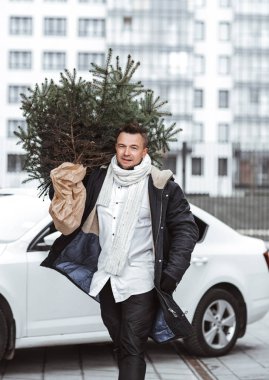 Sakallı genç adam şehir caddesinde bir Noel ağacı taşıyor. Babam eve yeni yıl hediyesiyle geliyor.