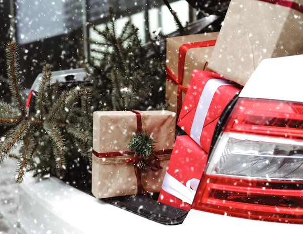 Car with trunk full of gift boxes, presents and fir tree for Christmas. Car, presents, craft box, snow, holidays. Street outdoor.