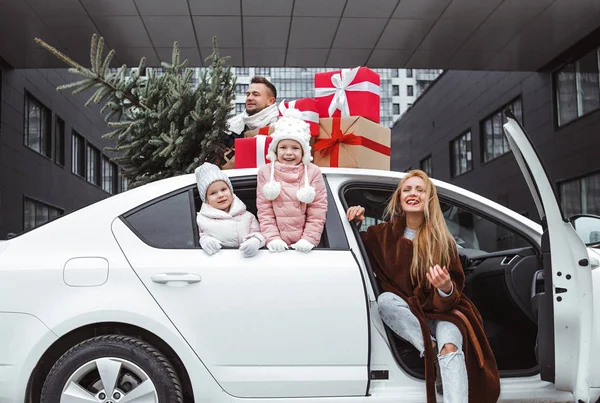 Christmas shopping and family preparation for winter holidays. Happy parents and cheerful children with many gifts and Xmas fir tree outside in the car.