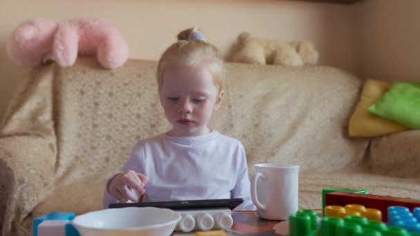 Μικρή Ξανθιά Παίζει Στο Τάμπλετ Και Τρώει — Αρχείο Βίντεο