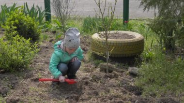 Bahçedeki bir çocuk spatulayla oynar, ağaç diker.