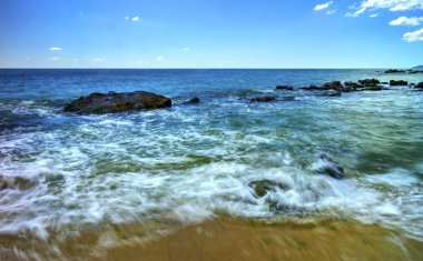 Güneşli bir sahilde kayalar ve deniz dalgaları olan güzel bir manzara.