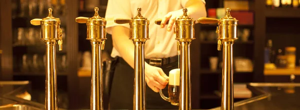 Cerveza de oro en la mano y grifos de cerveza — Foto de Stock