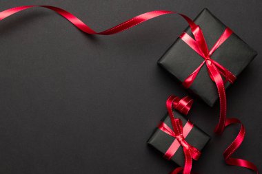 Yeni yıl geçmişi. Siyah arka planda kırmızı kurdeleli Noel hediyeleri. Xmas hediyesi. Kış tatili konsepti. Mutlu Noeller ve mutlu bayramlar tebrik kartı, çerçeve, bayrak