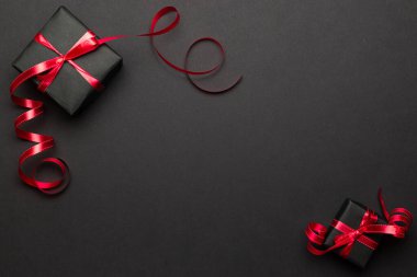 Yeni yıl geçmişi. Siyah arka planda kırmızı kurdeleli Noel hediyeleri. Xmas hediyesi. Kış tatili konsepti. Mutlu Noeller ve mutlu bayramlar tebrik kartı, çerçeve, bayrak