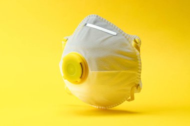 Sarı arka planda tıbbi güvenlik maskesi. Coronavirus hücresi Covid-19 virüsü önleme yolu ile korunuyor. Pandemik sağlık riski kavramı. Uçan patojen.