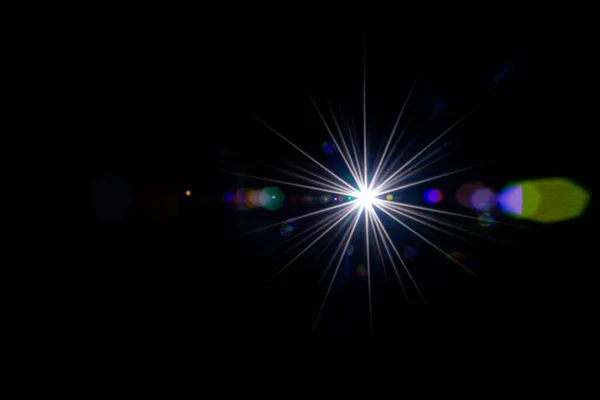 Rozbłysk tapety. Gwiazda lub słońce świecą światłem na obiektywie. Efekt błysku słonecznego na czarnym tle. Odbicie przecieku optycznego i abstrakcyjne światła bokeh. — Zdjęcie stockowe