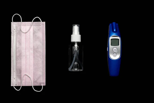 Surgical protective Mask isolated. Pandemic infection covid protection with Medical surgical mask, sanitizer gel, Electronic thermometer and lab gloves on black. Dangerous Chinese Novel virus COVID-19